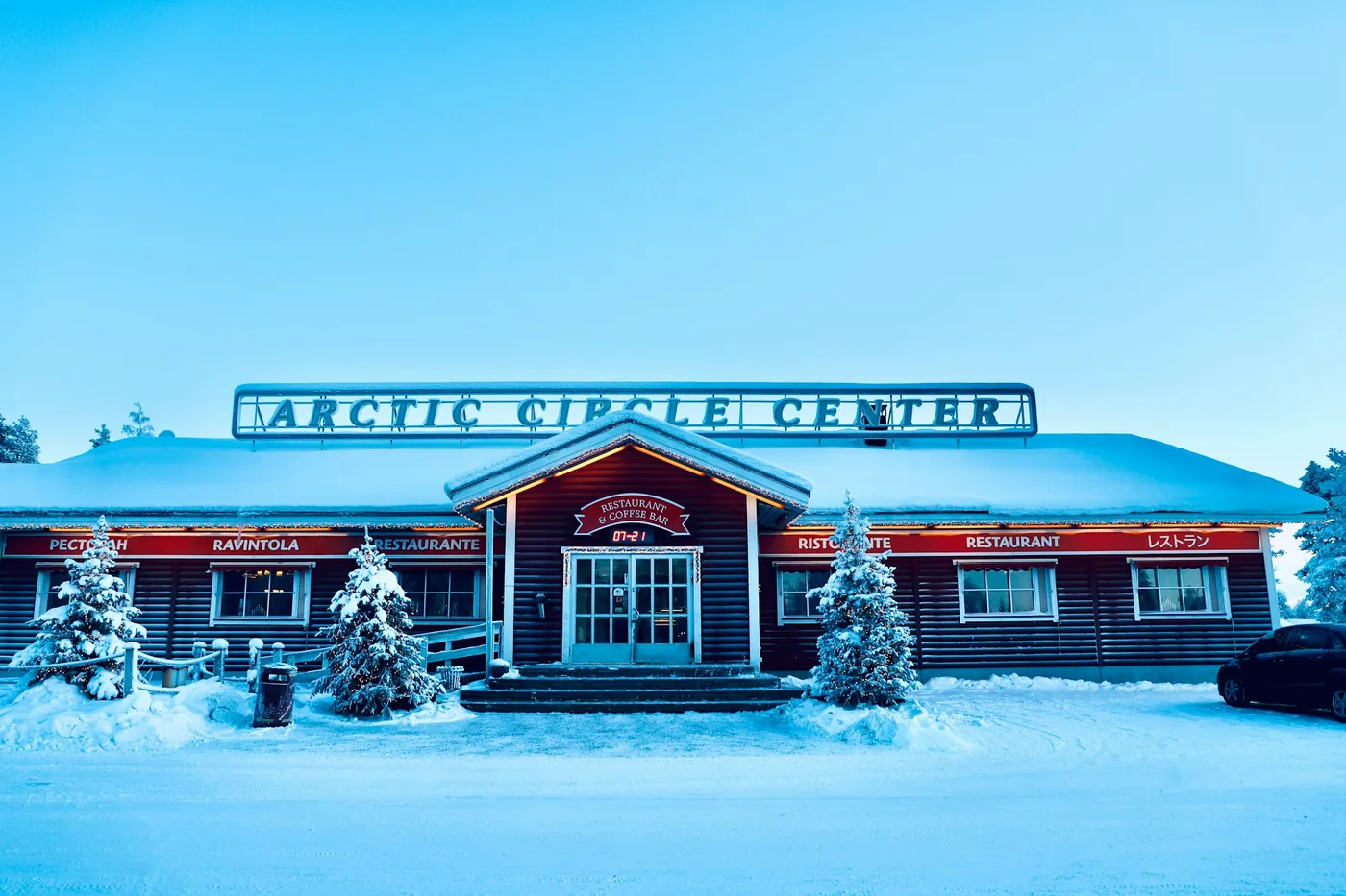 Houten gebouw met het opschrift Arctic Circle Center in de sneeuw, met besneeuwde sparren ervoor