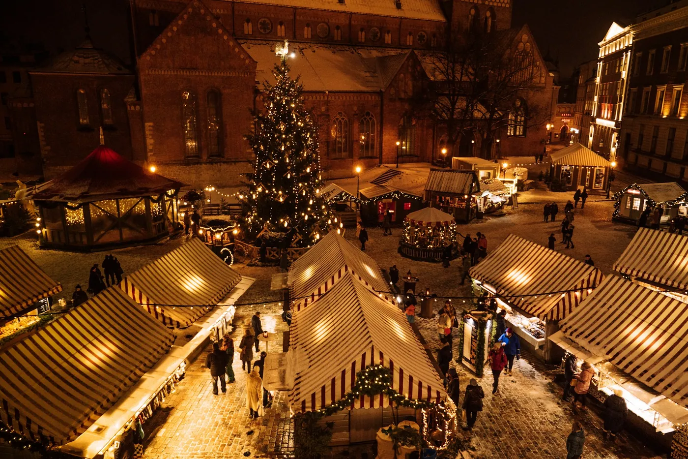 A Christmas market with lit stalls and a Christmas tree at night, seen from above