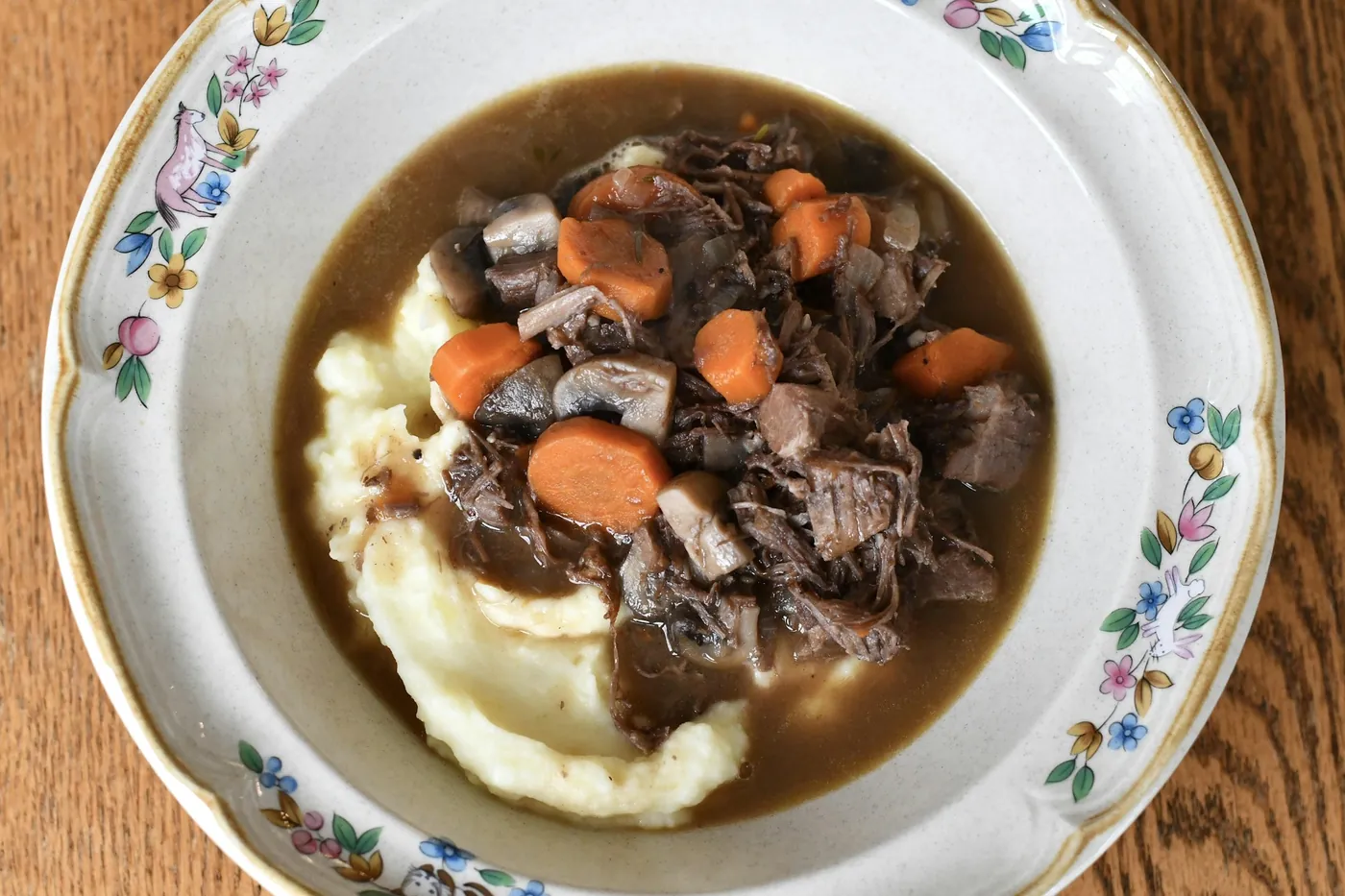 Guiso de carne con zanahorias y setas servido sobre puré de patatas
