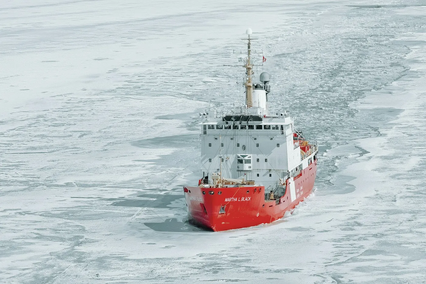 Un brise-glace rouge et blanc dans un chenal à travers la glace de mer, vu du ciel