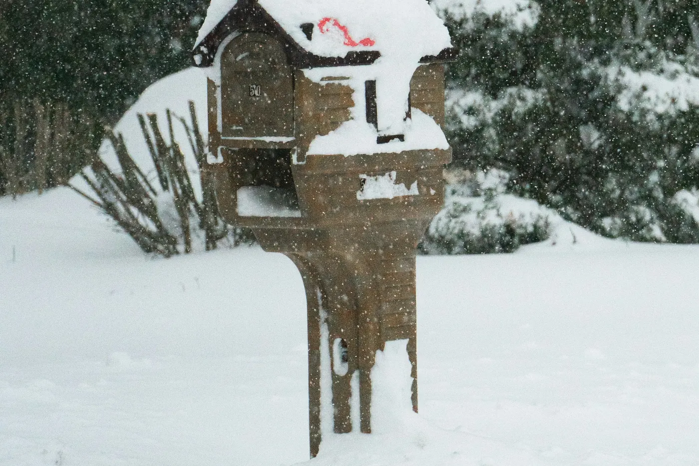 Una cassetta postale di legno con un cappello di neve in un giardino durante una nevicata