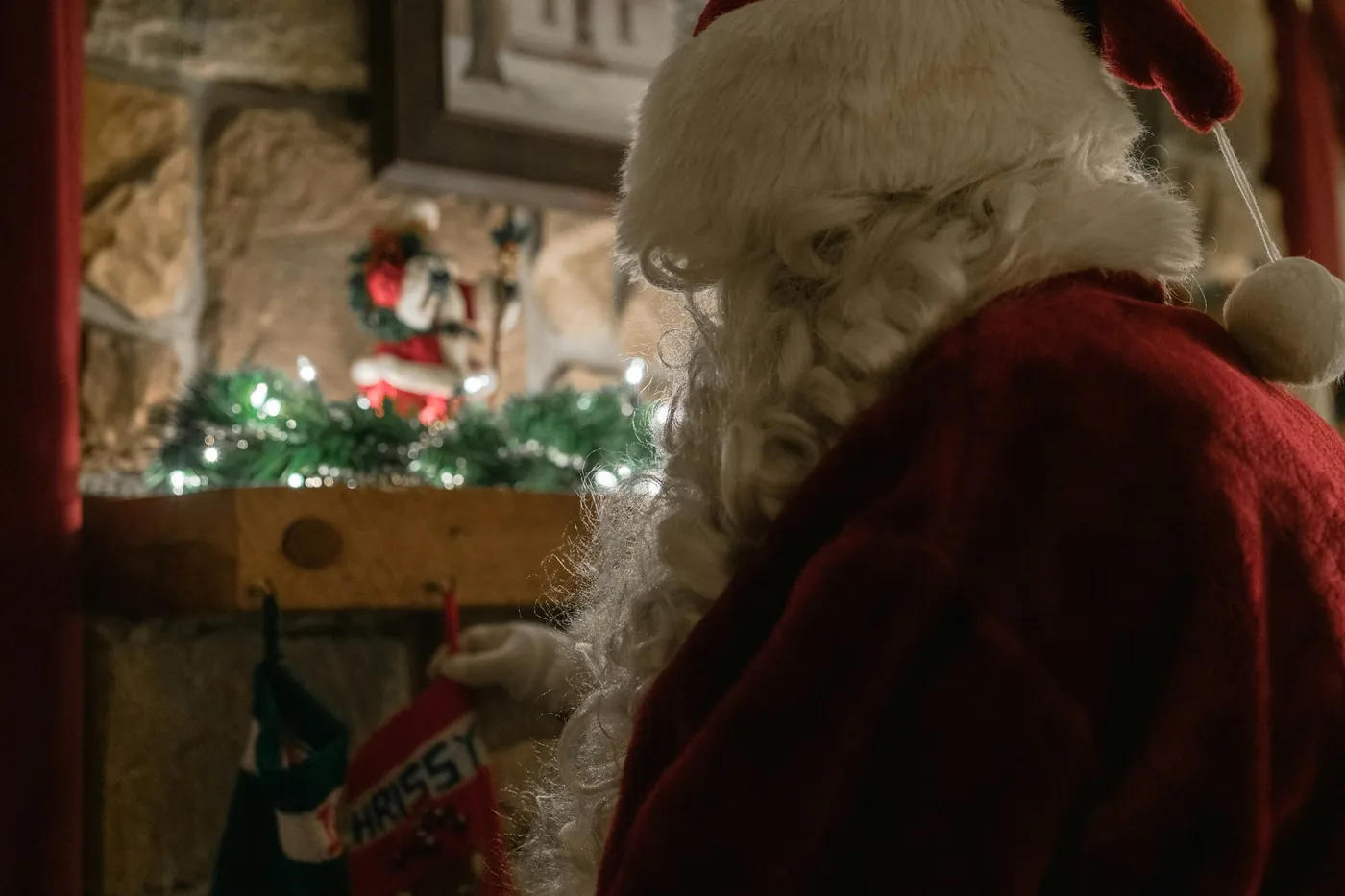 Eine Person im Weihnachtsmannkostüm von hinten an einem geschmückten Kamin mit Strümpfen