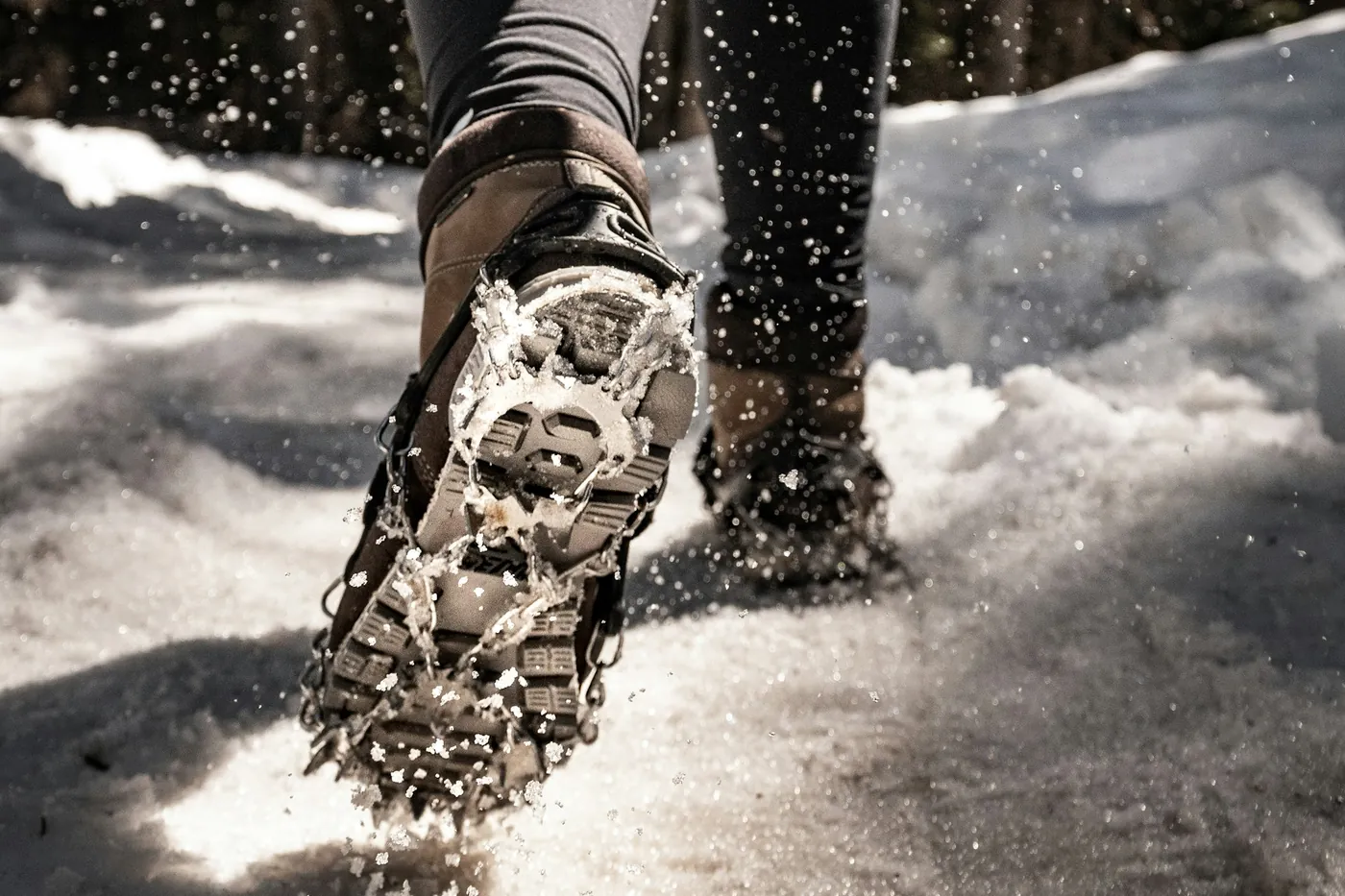 Wandelschoen met opschuifbare spikes op een besneeuwd pad, bomen op de achtergrond