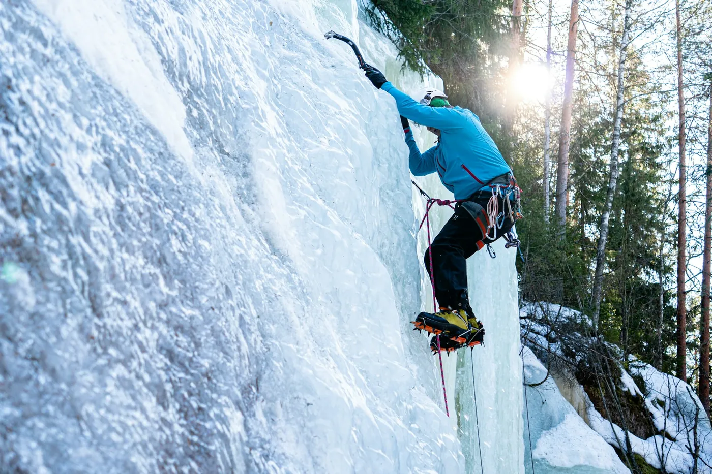 An ice climber on a frozen rock face next to conifer forest